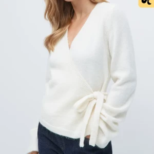 Kofta med knyte  - Superfin kräm vit omlottkofta med v-ringning och knyt i sidan. Koftan har långa ärmar och är stickad i ett mjukt material som känns riktigt cozy. Perfekt att styla med jeans för en clean look. Stl S I bra skick, lite nopprig på under sidan av armen 