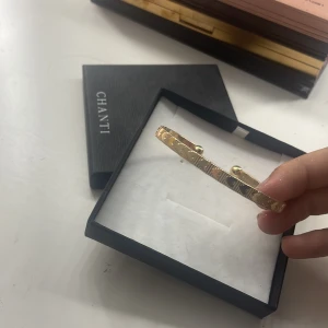 Guldfärgat armband med hjärtmönster CHANTI - Snyggt guldfärgat armband från CHANTI med ingraverade hjärtan och linjer runt hela bandet. Armbandet går att justera storleken på! 