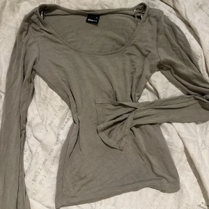 Långärmad topp - Snygg grå/ typ grön långärmad topp från Gina Tricot i storlek XS. Modellen har en rundad halsringning och är tillverkad i mjuk bomull. Ärmarna har en liten slitsdetalj vid mudden som ger en extra touch. Perfekt att styla med jeans eller kjol. Använt ca 2 gånger