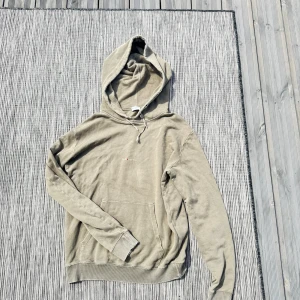 Beige hoodie från Saint Laurent - Snygg beige hoodie från Saint Laurent med broderad logga på bröstet. Tröjan har huva med snörning, känguruficka och långa ärmar. Tillverkad i mjuk bomull, perfekt för en chill och avslappnad stil.