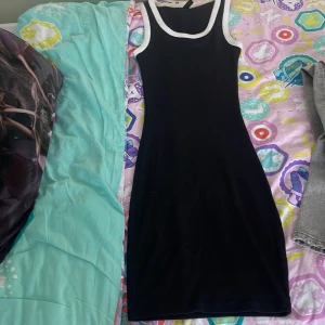 Svart ribbad klänning  - Snygg svart ribbad kortklänning från H&M Divided med vita kontrastkanter vid hals och ärmhål. Ärmlös och figurnära modell som ger en sportig och clean vibe. Perfekt för dig som gillar enkel men stilren look.