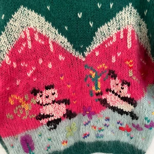 Grön stickad tröja med panda-motiv - Färgstark stickad tröja från Binomio i fluffig mohair- och ullmix. Framsidan har ett lekfullt motiv med pandor, blommor och hjärtan. Tröjan har rund hals och långa ärmar, perfekt för dig som gillar unika statement-plagg.