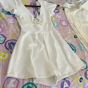 Vit dress från H&M Divided (INGEN KLÄNNING) - Supersöt vit kortdress från H&M Divided i storlek XXS. dressen har korta ärmar, v-ringning med snygg cut-out detalj framtill och en lätt utsvängd kjol/shorts. Perfekt för dig som gillar en enkel men trendig look. Väldigt chick och lyxig
