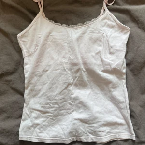 Ljus rosa linnetopp med spetskant - Söt ljus rosa linnetopp med tunna axelband och fin spetsdetalj längs urringningen😍. Toppen är i mjuk och har en enkel, rak passform som känns både fräsch och stilren. Perfekt att styla med jeans eller kjol för en clean look. Storlek M men passar även S!❤️