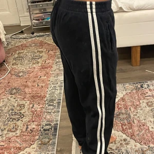 Mörkblå mjukisbyxor med vita ränder melville  - Mörkblå mjukisbyxor från brandy melville  med två vita ränder längs sidorna. Byxorna har resår i midjan, sidofickor och är tillverkade i ett mjukt material. Passformen är loose och de har en sportig vibe, perfekta för chill eller träning. Jag är 153 cm för referens. Passar allt från xs-m