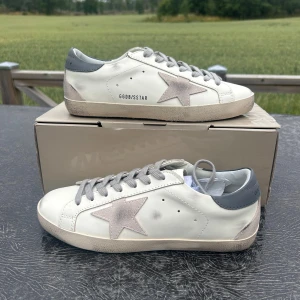 Golden Goose vita sneakers med stjärna - Golden Goose sneakers i vitt skinn med grå mockadetaljer och ikonisk stjärna på sidan. Grå snörning, grå hälkappa och beige sula med vintage-look. Klassisk rund tå och platt sula. Kommer med originalpåse och tags.