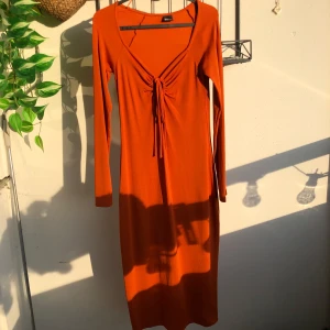 Orange långklänning  - Snygg orange långklänning med lång ärm och v-ringning. Mjuk och stretchig i materialet, och lite tjockare tyg så den kan användas året om typ. Använd en gång jag är 169 cm lång o den är t ca mitten av smalbenen på mig. Den är storlek S men den passar M oxå.