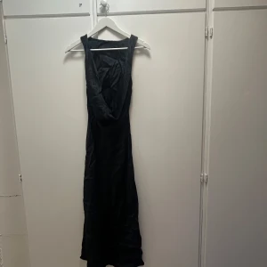 Svart långklänning med öppen rygg - Snygg svart långklänning i glansigt material med öppen rygg och breda axelband. Klänningen har en elegant och stilren siluett som faller fint längs kroppen. Perfekt för dig som vill sticka ut med en klassisk look. ( använt 1 gång ) nytvättad behöver stryckas 