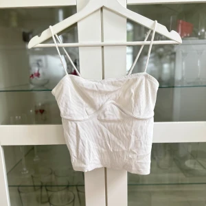 Vitt kort ribbat linne med detalj - Ett vitt kort ribbat linne med detalj under bysten från Ginatricot i storlek S. Köptes secondhand, har aldrig kommit till användning! FÖRST TILL KVARN!