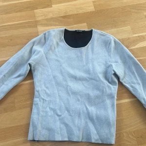 Glittrig silvertröja från Tiger of Sweden - Snygg långärmad tröja från Tiger i glittrigt silvermaterial. Tröjan har en rund halsringning och sitter figurnära. Perfekt för dig som vill sticka ut lite extra med en stilren men ändå festlig look. Liten i storleken