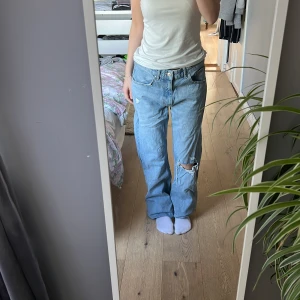 Ljusblå flare jeans från Bershka - Säljer ett par ljusblå jeans från Bershka med flare-ben och slitningar, inklusive en stor reva vid knät. Jeansen har klassisk femficksdesign och är tillverkade i bomullsdenim. Perfekt för dig som gillar en avslappnad och trendig look.