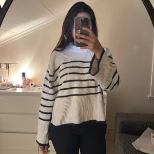 Vit och svart randig stickad tröja - Vit stickad tröja med svarta horisontella ränder och ribbade muddar. Tröjan har en relaxed fit med lite bredare ärmar och rund halsringning. Perfekt för lager-på-lager och chill stil.