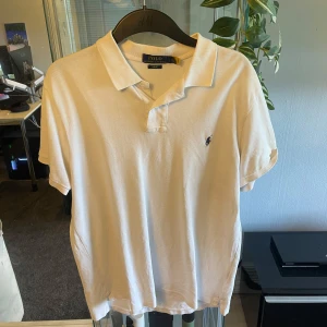 Vit pikétröja från Polo Ralph Lauren - Klassisk vit pikétröja från Polo Ralph Lauren med korta ärmar och broderad logga på bröstet. Tröjan har krage och knäppning framtill, tillverkad i mjuk bomull som känns skön mot huden. Perfekt för en clean och stilren look.