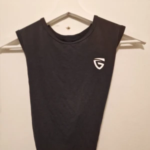 Svart träningstopp  - Svart linne med vit logga på bröstet. Toppen har öppen rygg med snygg knytning baktill som ger en cool look. Perfekt för träning eller när du vill ha en sportig vibe.