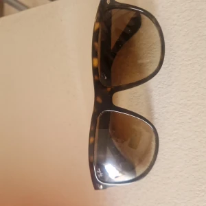 Ray-Ban solglasögon brunmelerad - Snygga Ray-Ban RB4147 solglasögon med brunmelerad båge i klassisk wayfarer-stil. Glasen är bruna och bågen har ett coolt sköldpaddsmönster. Perfekt accessoar för att lyfta din stil under soliga dagar.