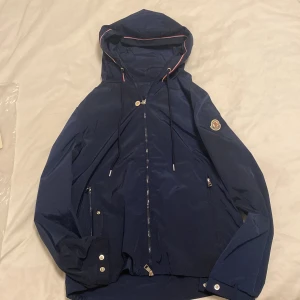 Windbraker från moncler - Snygg marinblå vindjacka från Moncler med huva och dragsko. Jackan har dragkedja framtill, två fickor med dragkedja och Moncler-logga på ärmen. Säljer den för att den är lite för stor för mig Storlek M. Allt funkar som de ska. Pris går att diskutera. Dm om mer. Nytt skick!!!