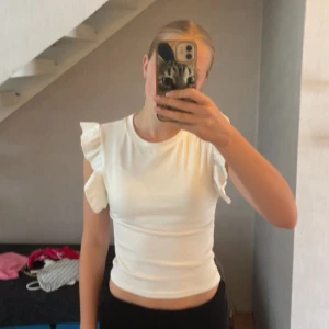 Vit croppad topp med volangärmar - Säljer en vit croppad topp med volangdetaljer på ärmarna. Toppen är figurnära och har en enkel, stilren design som passar perfekt till jeans eller kjol. Materialet känns mjukt och stretchigt, vilket gör den bekväm att bära hela dagen.🤍
