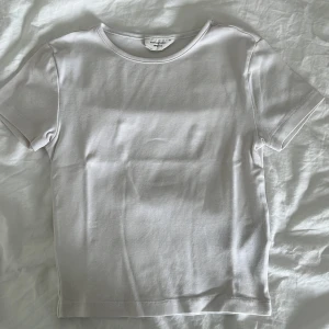 Vit basic t-shirt från Gina Tricot - En klassisk vit t-shirt från Gina Tricot, basically basics-kollektionen. T-shirten har rund halsringning, korta ärmar och är gjord i mjuk bomull. Perfekt att styla med jeans eller kjol för en clean och enkel look.