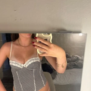 Rutig svartvit korsett med spets - Supersöt korsett med svartvitt rutigt mönster, justerbara axelband💋Toppen har hakknäppning i ryggen som finns i 2 olika lägen. Perfekt att styla med jeans eller kjol för en trendig look.
