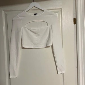 Vit croppad långärmad topp med cut out - Snygg vit croppad topp från shein med långa ärmar och en cool cut out-detalj över bröstet. Toppen är figurnära och har en stilren look som passar perfekt till höga jeans eller kjol. Materialet är mjukt och stretchigt för en bekväm känsla.