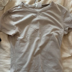 Beige t-shirt från H&M Divided - Enkel och stilren beige t-shirt från H&M Divided. Modellen har rund halsringning och korta ärmar, perfekt för en clean och avslappnad look. Tillverkad i mjuk bomull som känns skön mot huden.