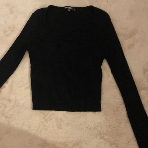 Svart ribbad tröja från Missguided - Svart ribbad långärmad tröja från Missguided med rundad, lite djupare halsringning. Modellen är tight och croppad, perfekt att styla med höga jeans eller kjol. Mjuk och stretchig, passar både till lager-på-lager och som den är.