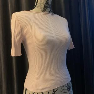 Ljusrosa ribbad topp från H&M - Supersnygg ljusrosa ribbad topp från H&M Divided. Modellen är figurnära med korta ärmar och en djup, rundad rygg som ger en extra touch. Toppen har en stilren, enkel design och är tillverkad i mjukt stretchigt material som sitter perfekt. Endast använd ett fåtal gånger och har inte sett några defekter. 