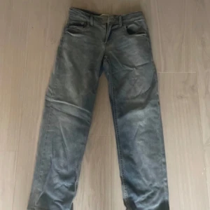 Levi's ljusgrå jeans straight fit - Säljer ett par ljusgrå Levi's jeans i klassisk straight fit. Jeansen har fem fickor, bälteshällor och den ikoniska läderpatchen bak. Perfekta för dig som gillar en avslappnad och tidlös look. Materialet är slitstarkt denim.