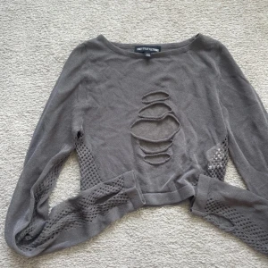 Grå stickad tröja PrettyLittleThing XS - Grå mesh tröja från PrettyLittleThing i storlek XS. Tröjan har coola slitningar framtill och meshdetaljer längs ärmarna. Långärmad och med en lite croppad passform som ger en edgy vibe. Perfekt för dig som gillar unika detaljer och streetstyle.