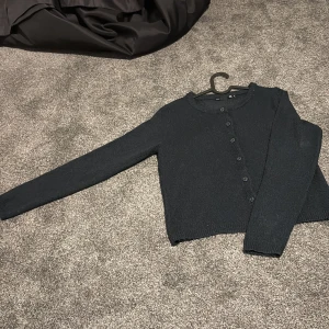 Svart stickad kofta från 157, S - Mysig svart stickad kofta från 157 med rund halsringning och knappar hela vägen framtill. Perfekt att slänga över en t-shirt eller linne. Långärmad och i klassisk modell som funkar till allt. Säljes pga att jag köpte två stycken