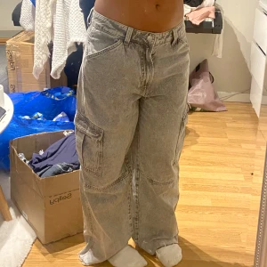 Grå cargojeans från H&M Divided - Säljer ett par grå cargojeans från H&M Divided i storlek 40. Endast använd en gång. Byxorna är sitter lågmidjat och baggy i passformen, stora sidofickor och en snygg tvättad look. Perfekta för dig som gillar loose och avslappnad stil. Materialet är jeans och de har klassiska cargodetaljer.