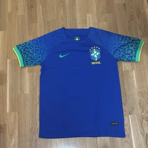 Blå Brasilien fotbollströja Nike - Snygg blå Brasilien fotbollströja från Nike med grönt Swoosh och CBF-emblem på bröstet. Ärmarna har leopardmönster i blått och grönt med gula detaljer vid ärmslut. 