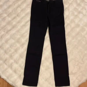 Mörkblå chinos från Tommy Hilfiger - Snygga mörkblå chinos från Tommy Hilfiger, modellen Bleecker Chino Stretch Slim Fit. Byxorna har smal passform, bälteshällor och bakfickor med knapp. Stretchigt material för extra komfort och stilren look. Perfekt för dig som gillar en clean och modern vibe. Inga defekter, använda ett fåtal gånger till högtider. Hör av er om frågor!❤️