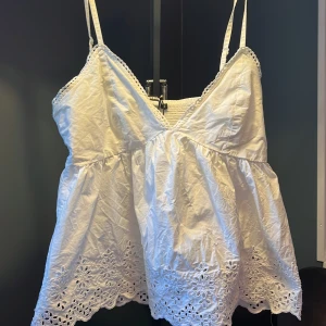 Vit broderad linnetopp från Bikbok - Supersöt vit linnetopp från Bikbok med smala axelband, v-ringning och broderade blommor längs fållen. Toppen har volangkant nertill och smockad rygg för extra komfort. Perfekt för varma dagar! Nypris 399 och är i bra skick