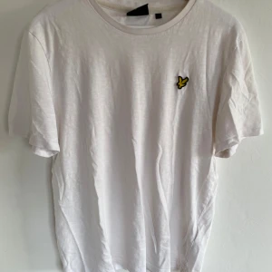 Vit t-shirt från Lyle & Scott - Vit t-shirt från Lyle & Scott med klassisk rund hals och korta ärmar. På bröstet sitter den ikoniska gula fågel-loggan. T-shirten är gjord i mjuk bomull och har en clean, enkel look som funkar till allt. Perfekt för dig som gillar stilrena plagg med diskret branding.