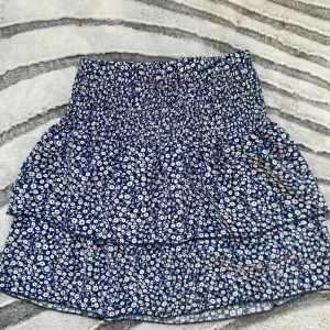 kjol / topp - Kan användas som både kjol och topp. Supersöt kort kjol från Emery Rose i blått med vitt blommönster. Kjolen har smockad midja och dubbla volanger som ger en flowy och trendig look. 