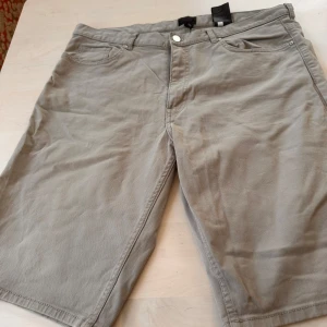 Beige shorts från H&M, strl 34 - Snygga beige shorts från H&M i klassisk femficksmodell. De har normal passform, midwaist och är gjorda i mjuk bomull. Perfekta för varma dagar och har både fram- och bakfickor samt knapp och dragkedja framtill.