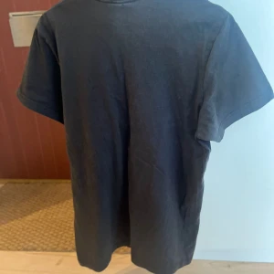 Svart Dsquared2 t-shirt med tryck - Svart t-shirt från Dsquared2 med rund hals och korta ärmar. Framsidan har ett stort tryck med kanadensisk flagga, text och broderade detaljer i rött, vitt och gult. Materialet känns som mjuk bomull och passformen är normal. Perfekt för dig som gillar statement-plagg.