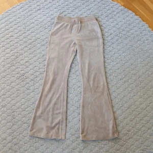 Beige mjukisbyxor från Lindex lågmidjade  - Supermjuka beige mjukisbyxor från Lindex med bootcut-ben och snörning i midjan. På ena benet finns ordet 'Love' i glittriga strasstenar som ger extra bling. Perfekta för chill dagar eller när du vill vara extra cozy.