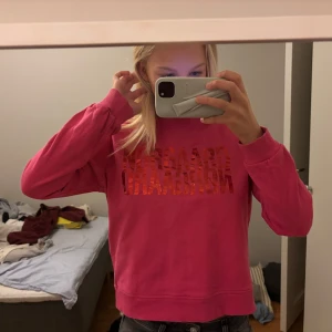 Rosa sweatshirt från Nørgaard - Säljer en rosa sweatshirt från Nørgaard med glansigt rött tryck på bröstet. Tröjan har rund hals, långa ärmar och ribbade muddar. Perfekt för dig som gillar färg och vill sticka ut lite extra.