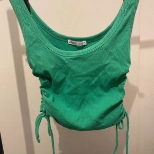 Grön ribbad linnetopp från Zara - Snygg grön ribbad linnetopp från Zara med dragsko och snörning i sidorna. Toppen är ärmlös och har en croppad passform som ger en fräsch och trendig look. Perfekt för varma dagar och enkel att matcha med jeans eller kjol.