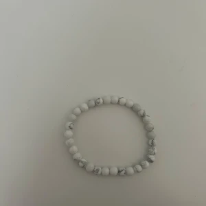 Vitt pärlarmband med marmormönster - Stilrent armband med runda vita pärlor och grå marmormönster. Elastiskt band gör det enkelt att ta på och av. Perfekt accessoar för en clean och modern look.