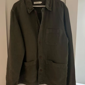 Olivgrön overshirt från Studio Total - Olivgrön overshirt från Studio Total i storlek L.               !!!! Nypris 899kr !!!   Skjortan har tre fickor framtill, knäppning med bruna knappar och klassisk krage. Tillverkad i ett svalt linnematerial, perfekt att bära som ytterplagg utanpp en hoodie eller likande eller enabart för sig själv. 