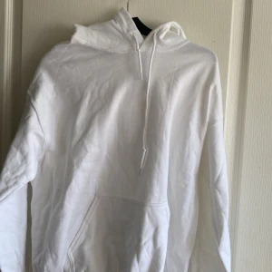 Vit hoodie med huva och magficka - Klassisk vit hoodie med huva och snörning samt stor magficka framtill. Tröjan har lång ärm och är tillverkad i mjuk bomull, perfekt för en avslappnad och stilren look.