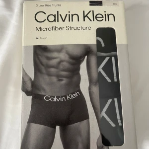 Svarta Calvin Klein trunks L - 3-pack svarta low rise trunks från Calvin Klein med vit logga på midjebandet. Tillverkade i stretchig mikrofiberpolyester som sitter skönt och följer kroppen. Perfekt för dig som gillar stilrena och bekväma underkläder med modern passform. Har kvitto