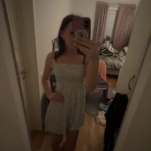 Vit blommig kortklänning från Sister - Supersöt vit kortklänning från Sister i storlek XS med blått blommigt mönster. Klänningen har smock upptill, tunna axelband och en flowy kjol. Perfekt för varma dagar och har en fräsch, ungdomlig vibe. Materialet känns lätt och bekvämt mot huden.