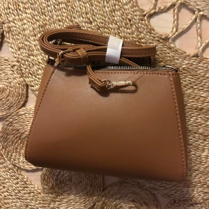 Brun handväska - Fin brun liten väska med axelband. Helt oanvänd. Följde med i en större väska som jag använder. Säljer likadan i vit! Från Zalando märket Even & Odd. Allt ska bort så kom med prisförslag!🌺🌺