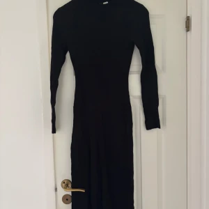 Svart ribbad långklänning med slits - Säljer en svart långklänning med ribbad struktur och lång ärm. Klänningen har en snygg slits framtill som ger extra edge och är figurnära i modellen. Perfekt för dig som gillar minimalistisk stil och vill ha något enkelt men ändå coolt.