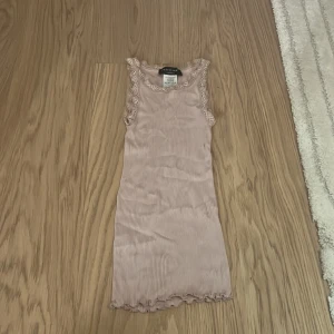 Ljusrosa ribbad linnetopp Rosemunde - Supersöt ljusrosa ribbad linnetopp från Rosemunde med spetsdetaljer vid ärmhål och halsringning. Toppen är ärmlös och har en feminin volangkant nertill. Materialet är en lyxig mix av silke och bomull som känns mjuk mot huden.