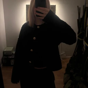 Svart teddyjacka med guldknappar - En fin svart kofta från Gina med guldiga detaljer🤩den är lite teddy i materialet. Storlek M men passar även s om man gillar de lite oversized